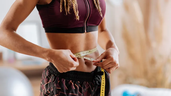 Slim woman wearing sport shorts and top measuring her waistline