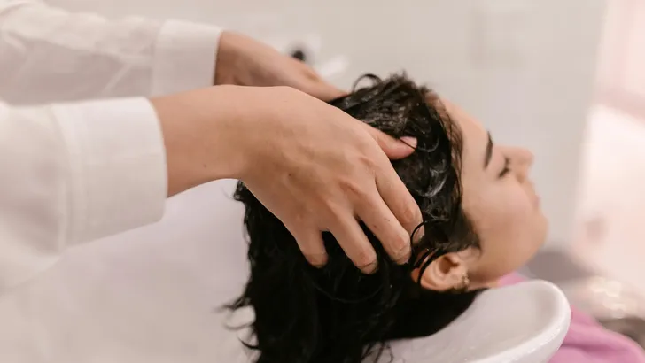 Meest gemaakte fout bij haren wassen – Foto van vrouw zittend bij kapper met hoofd in wasbak.