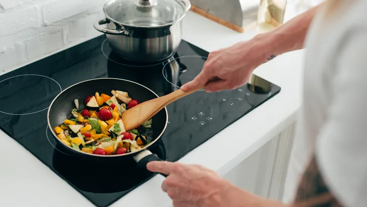 cropped shot of man cooking vegetables in frying pan on electric stove