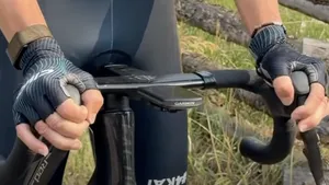 Een close-up foto van de handen van een wielrenner die de bovenkant van de shifters verticaal vastpakken in de 'skistok-houding', met een wazige bergachtergrond.