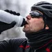 Close-up van een winterfietser die uit een met rijp bedekte bidon drinkt, met zichtbare adem in de koude lucht.