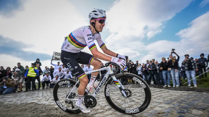 Tadej Pogačar rijdt in regenboogtrui over natte kasseien tijdens een winterse verkenning van Parijs–Roubaix.”