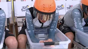 Drie wielrenners van de INEOS Grenadiers wielerploeg zitten naast elkaar op stoelen met hun armen diep in transparante bakken met ijswater om hun lichaam te koelen voor de start van de ploegentijdrit in de Tour de France.