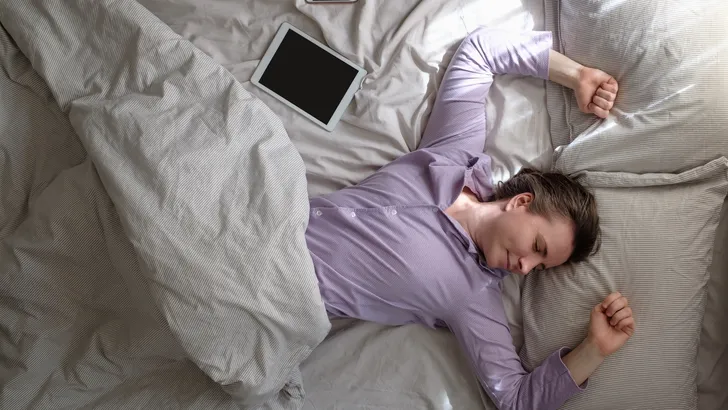 Vrouw ligt in bed naast tablet en telefoon