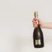 Vrouw houdt champagnefles voor een lichte achtergrond omhoog.