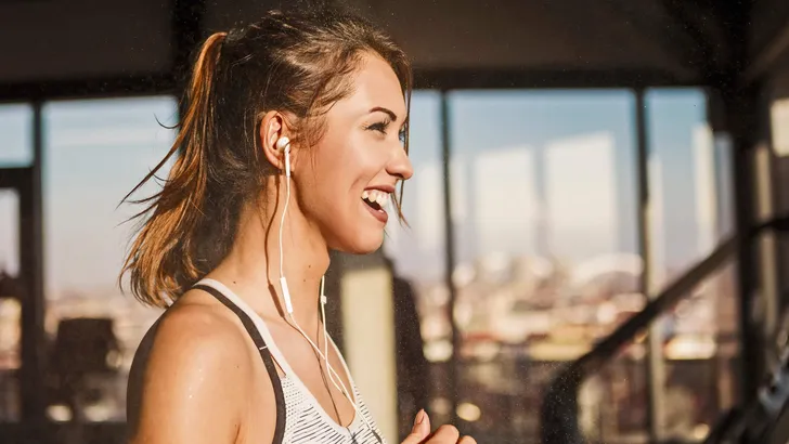 Happy sweaty woman running on treadmill in a gym