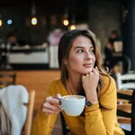 Stylish young woman drinking coffee at the cafe, looking away.