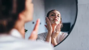 Een vrouw wast haar gezicht voor de spiegel en brengt cleanser aan op haar wangen.