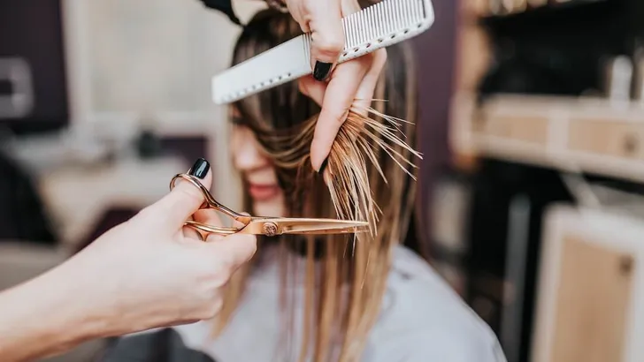 Beautiful young woman getting her haircut by a hairstylist at a beauty salon.