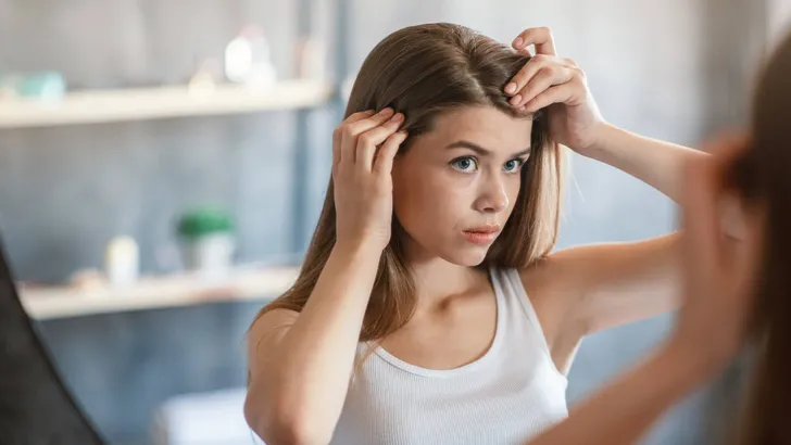 Pretty girl with hair loss problem looking in mirror at home