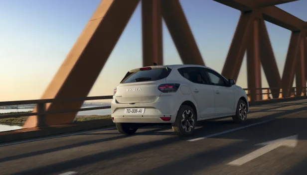 Achterzijde van een witte Dacia Sandero die over een stalen brug rijdt.