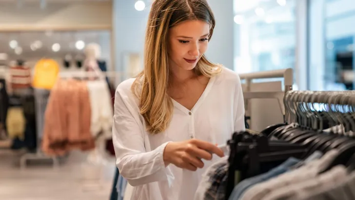 Happy young woman buying new clothes in store. Sale shopping fashion and people concept