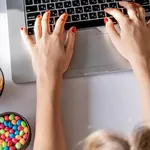 Girl works at a computer and eats fast food. Unhealthy food: chips, crackers, candy, waffles, cola. Junk food, concept.