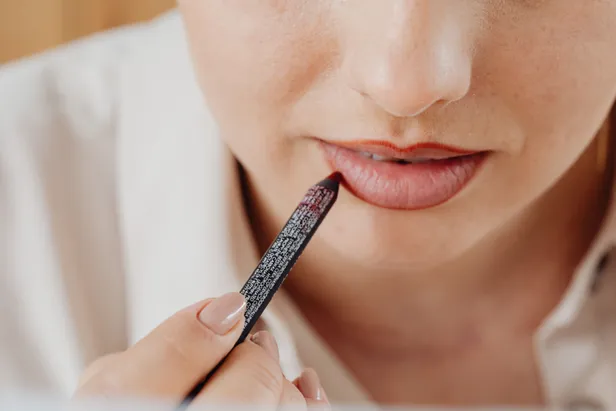Vrouw brengt een donkerrode lip liner stain aan op haar lippen. 