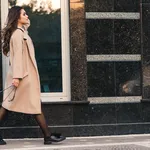 Fashionable woman with long hair walking in the city. Woman wears trendy coat and shoes.