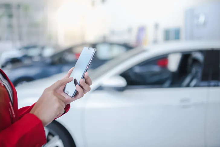Autodealer bekijkt online aanbod tweedehandsauto's en ex-leaseauto's op smartphone.