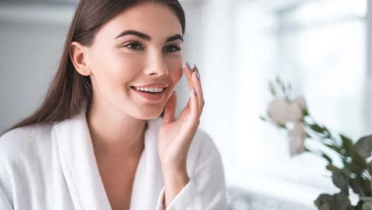 Satisfied girl doing face treatment in morning