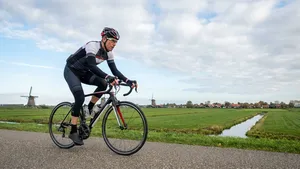 Een mannelijke wielrenner op een racefiets in een dynamische en efficiënte fietshouding op een landweg, die het resultaat van een correcte zadelhoogte illustreert.