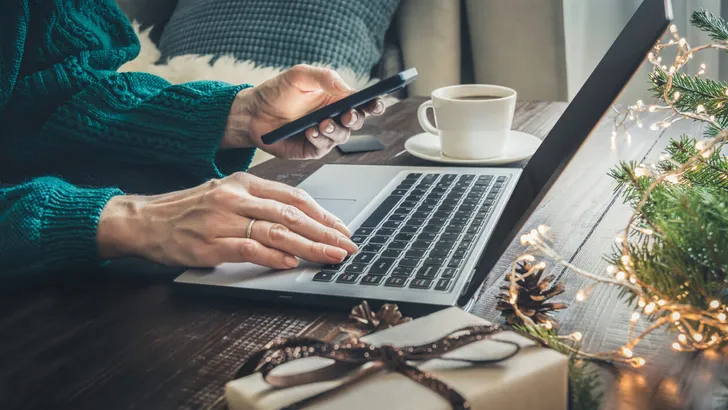 Christmas sales. Woman shopping with smartphone by laptop in home interior. Xmas. Planning holidays.