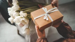 The child's hands hold a beautiful gift box with a ribbon and white tulips. Top view, close-up. Happy mother's day