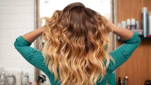 Dit kapsel zorgt voor extra volume bij fijn haar. – Foto van vrouw met lang golvend haar voor spiegel.