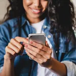 Cropped shot of an african-american young woman using smart phone at home. Smiling african american woman using smartphone at home, messaging or browsing social networks while relaxing on couch