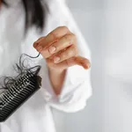 woman losing hair on hairbrush in hand on bathroom background