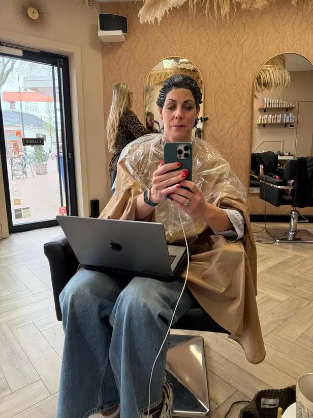 Hoofdredacteur Annelies in de kappersstoel met laptop op schoot 