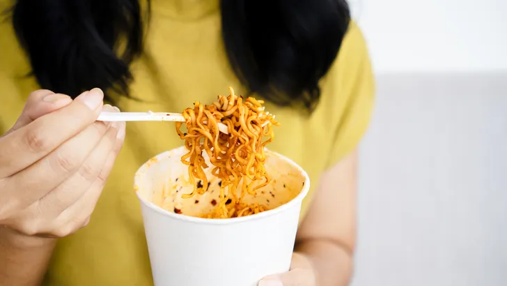 woman hand holding cup of spicy noodles, a woman eating noodle