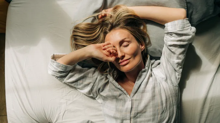 Vrouw rekt zich uit in bed na een nacht slapen.