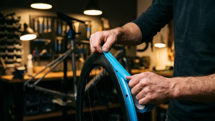 Een fietser zonder helm trekt in zijn werkplaats met kracht tubeless velglint strak over zijn velg.