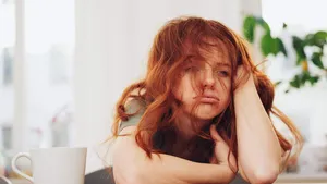 Red-haired girl sitting at table with boring face