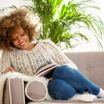 attractive african american woman sitting on sofa reading book