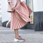 Pleated skirt coral color and sneakers. The girl is very dynamic posing on the street, the skirt is developing.