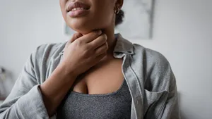 Bijgesneden afbeelding van een jonge vrouw van gemengde afkomst die thuis haar keel aanraakt.