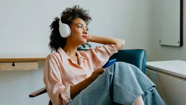 Relaxed Young Woman with Headphones on, Sitting in an Armchair and Listening to her Favorite Podcast