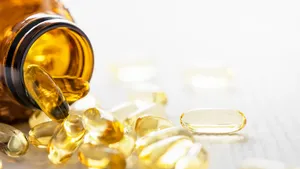 Many nutritional health supplement fish oil capsules spilling out of their bottle onto a white wood table background, shallow depth of focus.