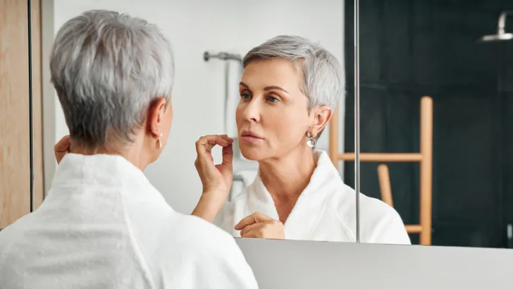 Beautiful senior woman wearing bathrobe standing in front of a mirror