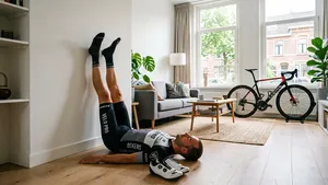Een mannelijke wielrenner in fietskleding ligt zonder helm in de woonkamer met zijn benen verticaal tegen de muur om te herstellen.