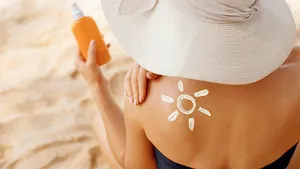 Vrouw die op het strand zit en zonnebrand vasthoudt