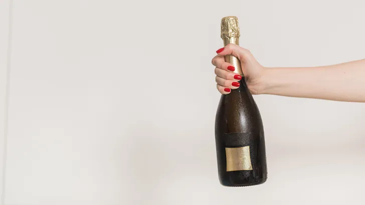 Vrouw houdt champagnefles voor een lichte achtergrond omhoog.