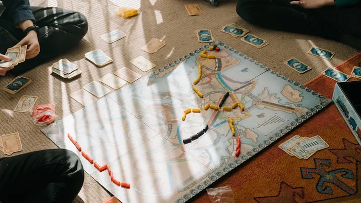 Mensen op de grond rond bordspel Ticket To Ride