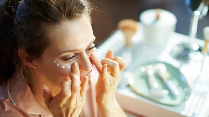 female at modern home in sunny winter day applying eye cream