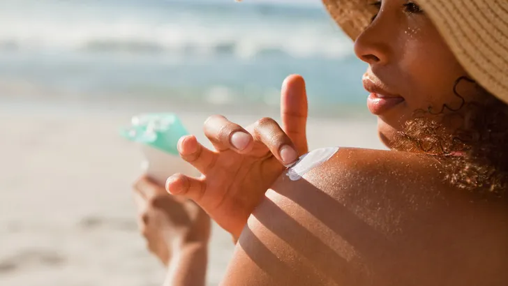 Young attractive woman attentively applying sunscreen on her sho