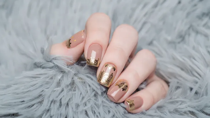 beige Nude manicure with gold lace pattern on a gray background