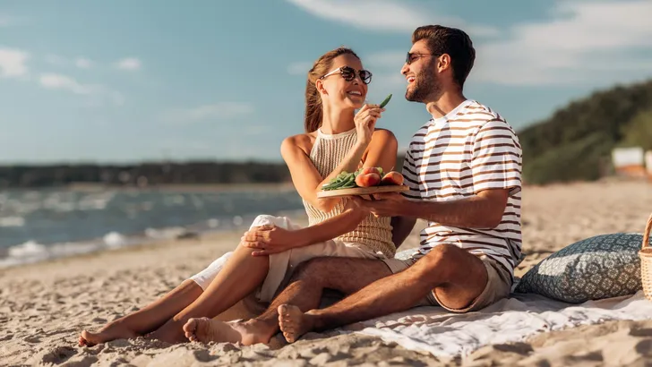 happy couple with food having picnic on beach