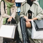 Crop women sitting on bench with shopping bags