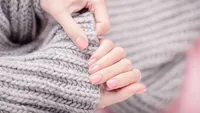 Female hands holding large gray woolen scarf. Manicure with pink color nail polish, shiny design. Top view