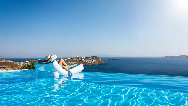 Foto van vrouw op opblaasbed aan rand van infinity pool met uitzicht over zee.