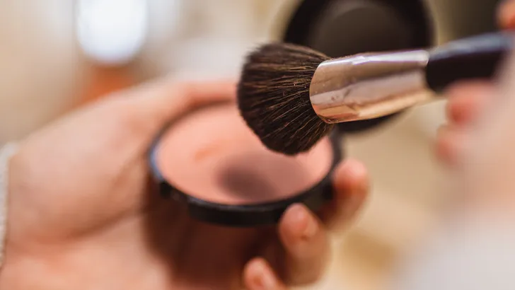 Detail van de handen van een vrouw die blush en een make-upkwast vasthouden.